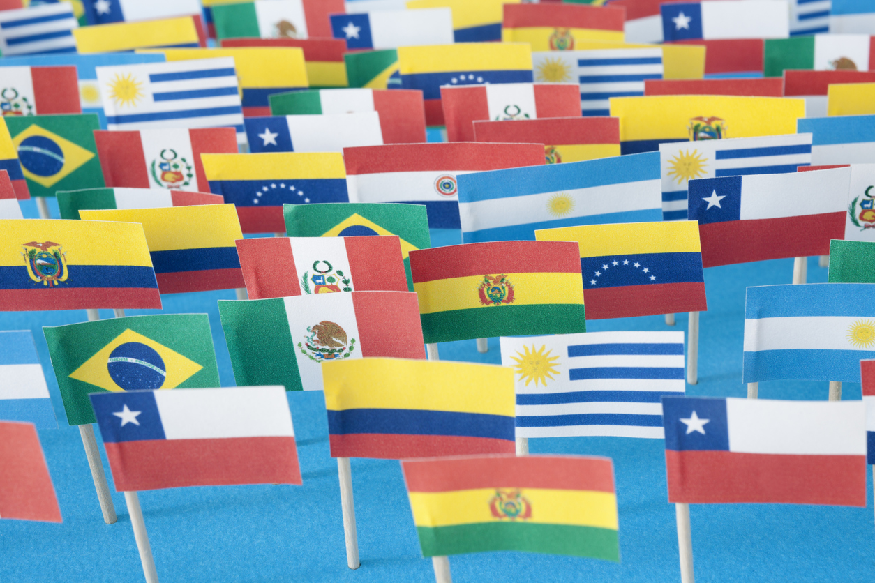 Lots of small handmade flags of latin american countries over blue background